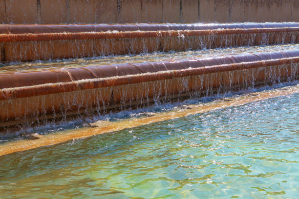 A close-up view of a smooth water fountain surface with ripples, surrounded by a blurred outdoor garden scene