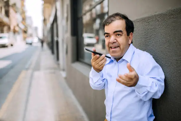 Photo of Mid-adult businessman with dwarfism recording voice message on his mobile phone
