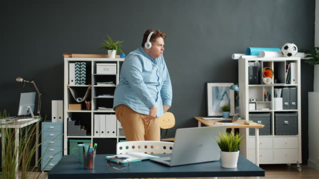 Slow motion of funny employee dancing in office room wearing headphones
