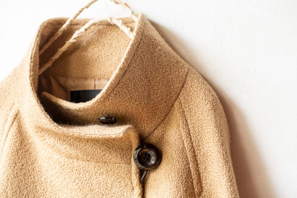 istock beige wool coat hanging on clothes hanger on white background. 1201592257
