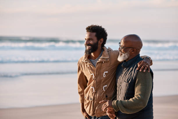 You're never too old to need your dad Shot of a young man going for a walk along the beach with his father arm around photos stock pictures, royalty-free photos & images