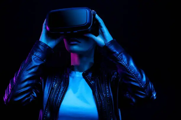 Photo of Young african american girl playing game using VR glasses, enjoying 360 degree virtual reality headset for gaming, isolated on black background in neon light