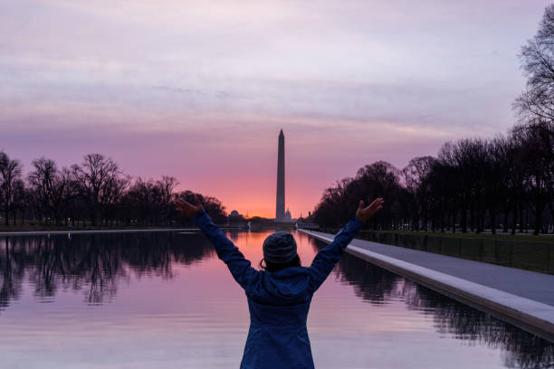 A woman with arms raised admiring Washington Monument, Sunrise sky in Washington DC A woman with arms raised admiring Washington Monument, Sunrise sky in Washington DC washington monument reflecting pool stock pictures, royalty-free photos & images