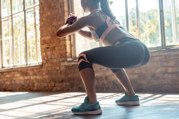 joven fit deportivo atleta activa mujer usar ropa deportiva agachada haciendo sentadillas sesión de entrenamiento de fitness piernas glúteos ejercicio ejercicio en el espacio de gimnasio soleado moderno en interiores, trasera de cerca vista - muscular build fotos fotografías e imágenes de stock