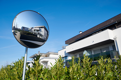 Road convex mirror with reflection of modern apartment houses and clear sky.
