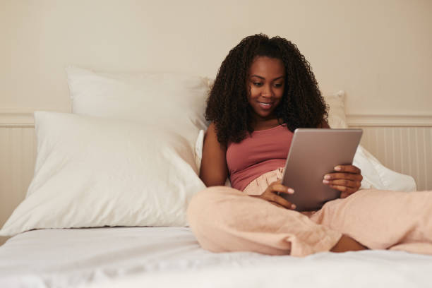 Young woman smiling while using a digital tablet in bed