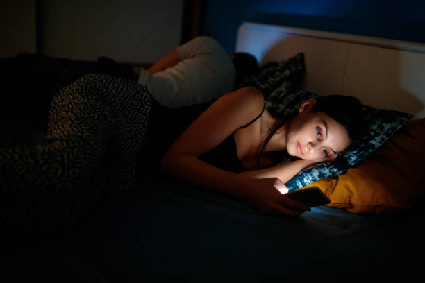 She is checking her smartphone at bedtime Young woman sending text message as her boyfriend sleeps in the bed, dark, copy space insomnia photos stock pictures, royalty-free photos & images
