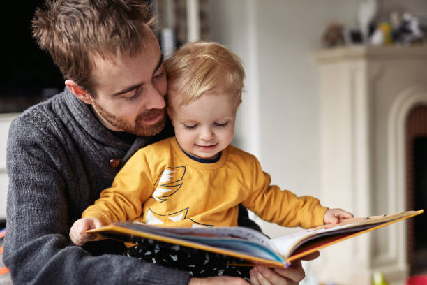 I'm gonna read this whole book today Cropped shot of an adorable little boy reading a book while sitting with his father at home belgium photos stock pictures, royalty-free photos & images