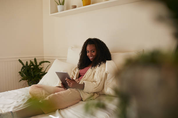 istock Smiling young woman relaxing on her bed with a digital tablet 1201610545