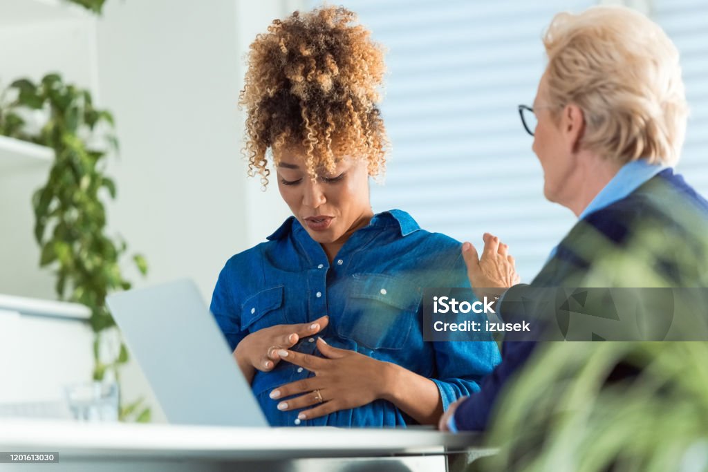 Elderly colleague talking to pregnant professional Elderly colleague talking to pregnant businesswoman sitting with hands on stomach. Business professionals are discussing in office. They are communicating at workplace. 35-39 Years Stock Photo