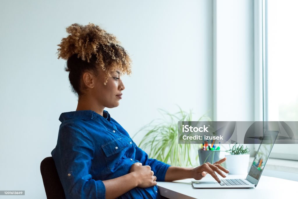 Pregnant expertise working on new business plans Side view of pregnant expertise working on new business projects at desk. Female professional is using laptop in office. She is wearing business casuals. 35-39 Years Stock Photo