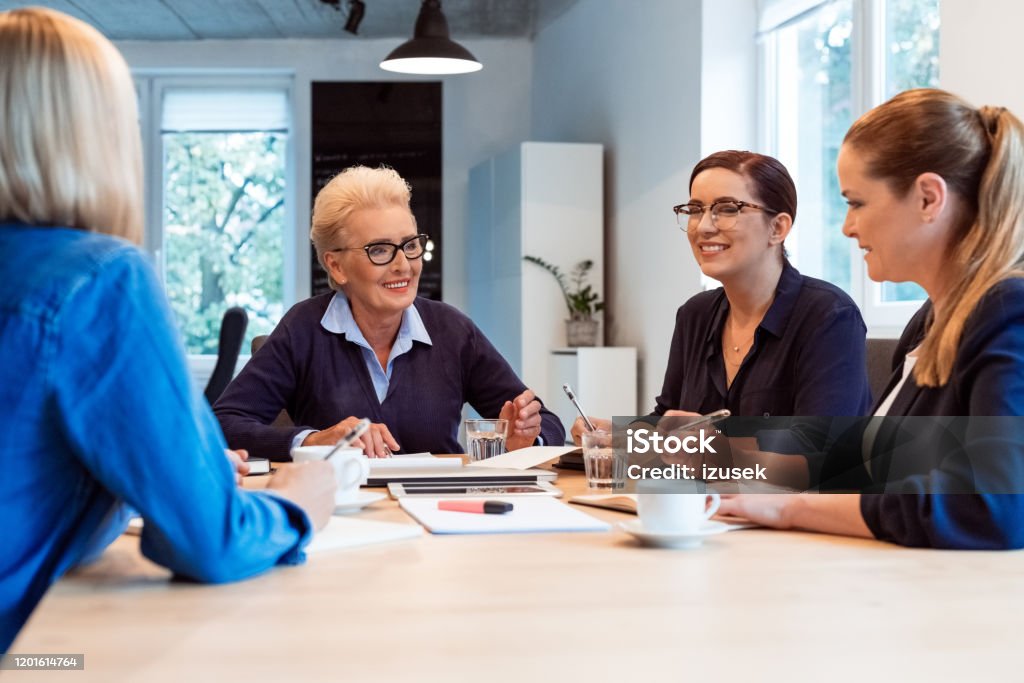 Smiling businesswomen discussing in office meeting Smiling female professionals discussing in meeting. Senior businesswoman planning with colleagues. They are running start up business. 35-39 Years Stock Photo