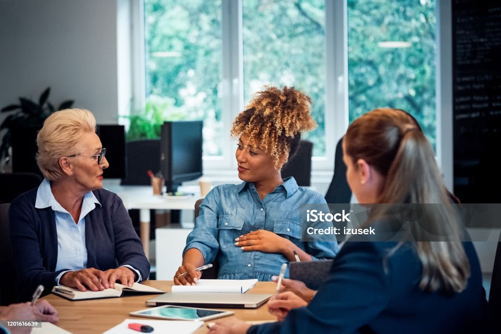 Elderly executive talking to pregnant colleague Elderly female executive talking to pregnant colleague. Businesswomen are brainstorming at desk. Business professionals are working in new office. 35-39 Years Stock Photo