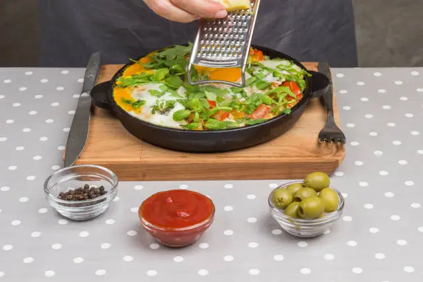 Photo of Stewed eggs and vegetables in pan. shakshuka for breakfast. Hand grate cheese