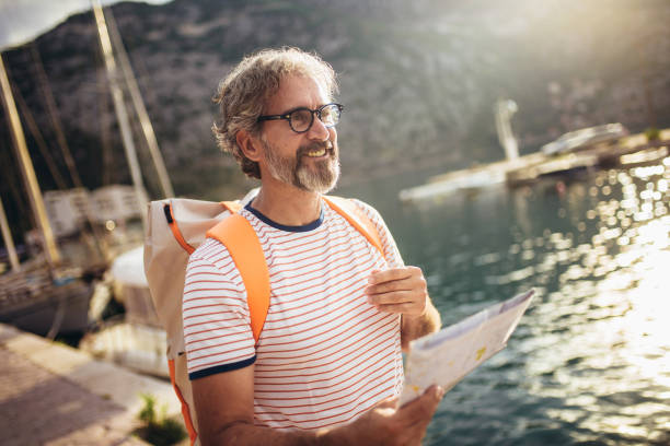 Tourist mature man standing with map and backpack near the sea.