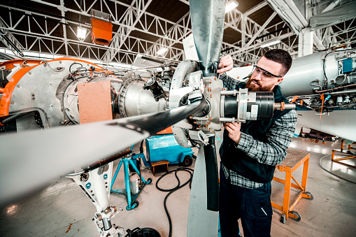 Aircraft engineer repairing a small front-engine airplane propeller disassembled in a hangar.