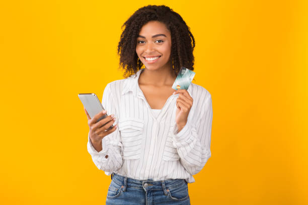 sonriendo afro mujer sosteniendo tarjeta mirando a la cámara - greeting card holding women credit card fotografías e imágenes de stock