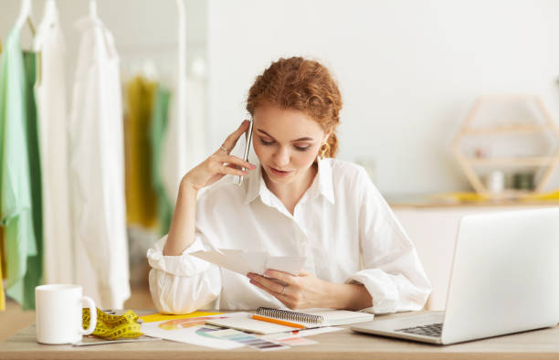 istock Young dressmaker talking by phone with customer, discussing order 1201618543