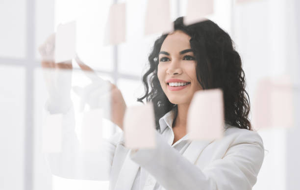 istock Smiling brazilian manager writing on sticky notes on window 1201619696