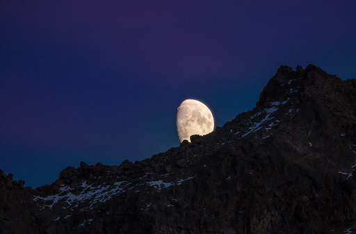 An almost full moon rises above some snow covered peaks near Telluride Colorado.