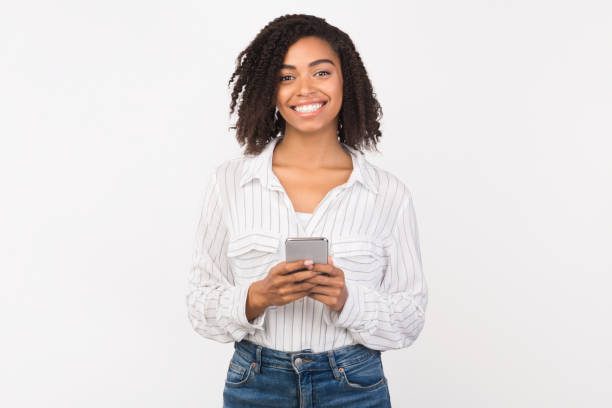 smiling afro girl using cell phone looking at camera - adult black camera caucasian imagens e fotografias de stock