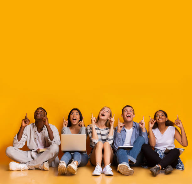 excited multiracial students pointing up at copy space - people in a row group of people in a row togetherness imagens e fotografias de stock