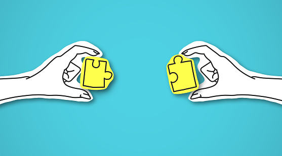 Two hands with yellow shining puzzles over blue background as symbol of collaboration