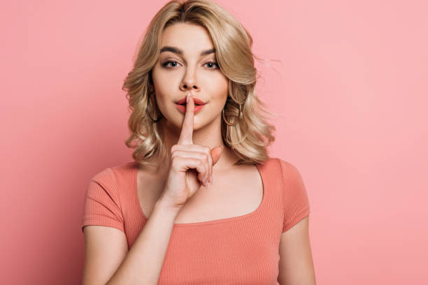 istock attractive girl looking at camera while showing hush gesture on pink background 1201624847