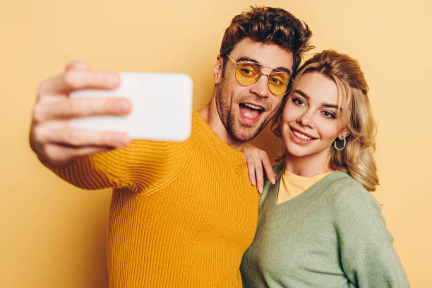 istock excited man taking selfie on smartphone with attractive girlfriend on yellow background 1201624854