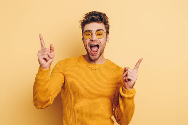 istock excited young man pointing with fingers while looking at camera on yellow background 1201624864