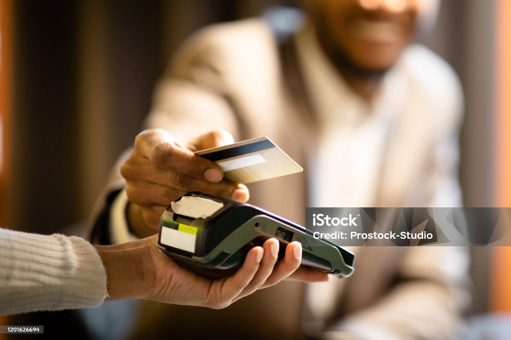 Afro businessman giving credit card to barman NFC Technology. Close up of black manager smiling, giving credit card to waitress paying with gold credit card in cafe Paying Stock Photo