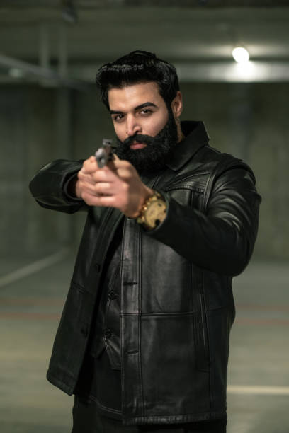 istock Assassin or terrorist in black leather jacket directing handgun on rival 1201627438