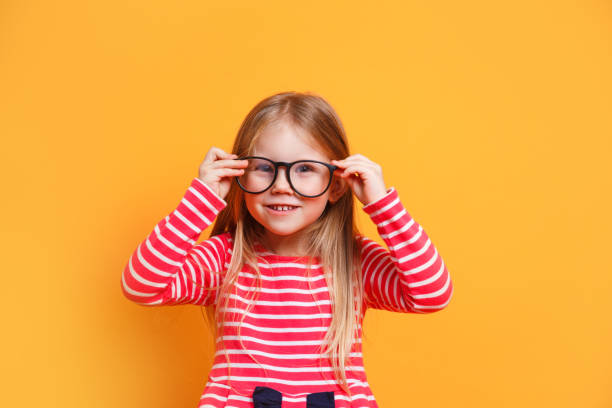 Portrait of young smiling girl wearing glasses on yellow background Portrait of young smiling little girl wearing glasses on yellow background nerd kid stock pictures, royalty-free photos & images
