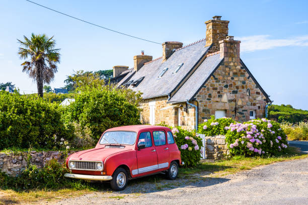 A classic french car parked in front of a typical granite house in Brittany, France. Plougrescant, France - August 3, 2019: A Renault 4 classic french car is parked in front of a typical granite house in Brittany with slate roof, palm tree and hydrangea by a sunny summer day. brittany france photos stock pictures, royalty-free photos & images