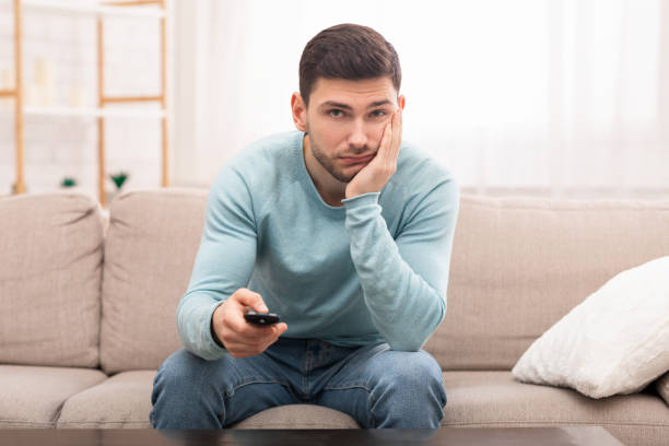 istock Bored Guy Switching Channels Watching TV Sitting On Couch Indoor 1201632399
