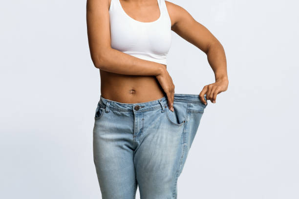 Young black woman wearing too large jeans Cropped of afro woman wearing too large jeans, demonstrating weight loss, effective diet concept too thin stock pictures, royalty-free photos & images