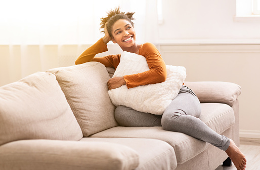 Weekend. Cheerful Black Girl Sitting On Couch Hugging Pillow Relaxing At Home On Weekend Morning. Empty Space