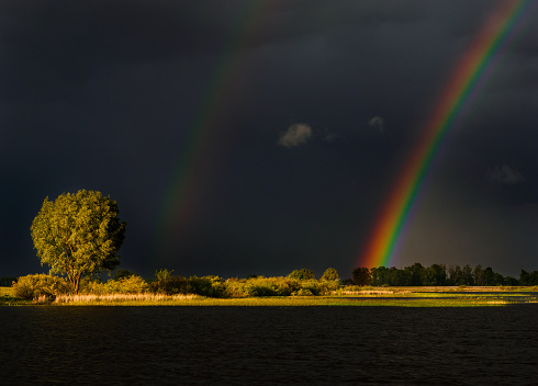 Rainbow in midsummer over the lake in beautiful landscape.