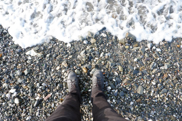 istock Man in black winter boots standing on a pebble beach 1201650988