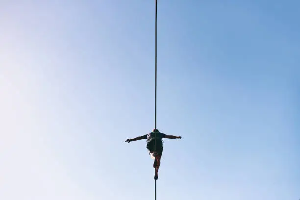 Photo of Young Caucasian slackline man practicing slackline against the sky on a clear summer day