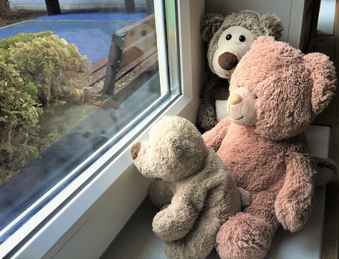 Family of Teddy bears sit on the windowsill and look out through the window at the playground