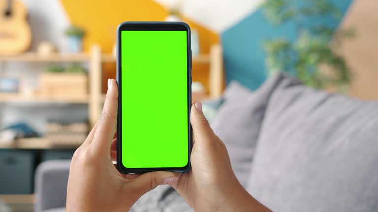 Close-up shot of green screen template smartphone in female hands at home, girl is watcing content without touching gadget screen. Modent technology and information concept.