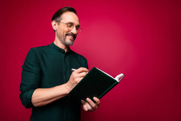 istock Photo of cheerful confident handsome man noting down information needed to develop business successfully isolated red vibrant color background 1201655235