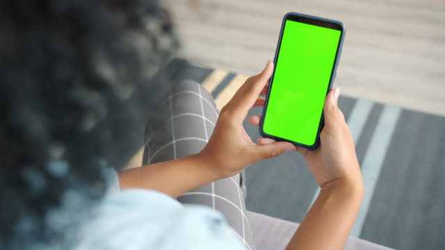 Back view of brunette holding chroma key green screen smartphone watching content