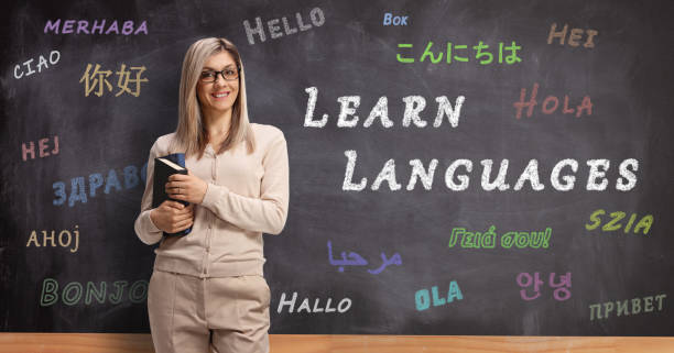 istock Young female language teacher standing in front of a blackboard with hello in different languages 1201655268