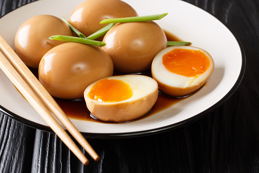 Soft-boiled eggs of nitamago in soya marinade with green onions close-up in a plate on the table. horizontal