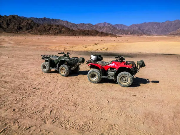 Two ATVs against the backdrop of mountains in the South Sinai Desert near Sharm El Sheikh (Egypt). Red and black quadricycles are standing on the sand, the concept of a tourist excursion  on quads