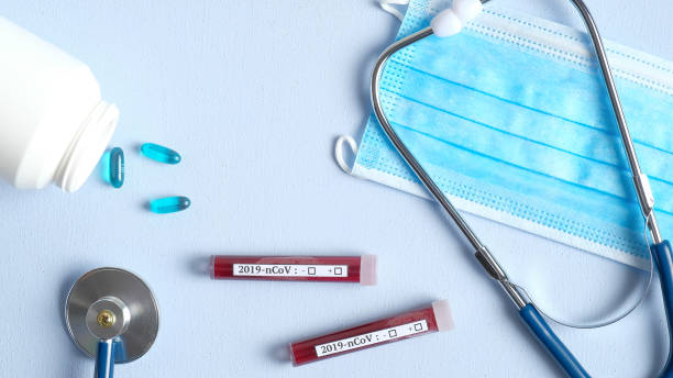 istock Coronavirus blood analysis concept. Laboratory table with respiratory mask, stethoscope, test tubes with blood, pills. 2019-nCoV Coronavirus originating in Wuhan, China. 1201659320