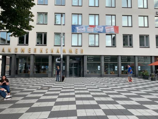 Kassel, Germany - August, 5 - 2019:  People sitting and walking in the city. Building belongs to the local chamber of trade. Poster on the second window row says „Offen für Vielfalt: = Open to diversity“.
