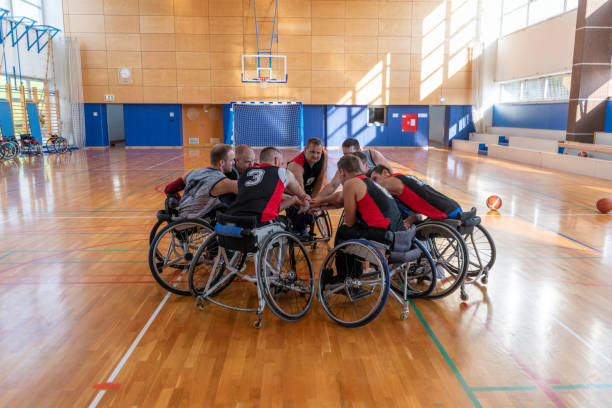Wheelchair players sitting in a circle and clasping hands in a school gymnasium.